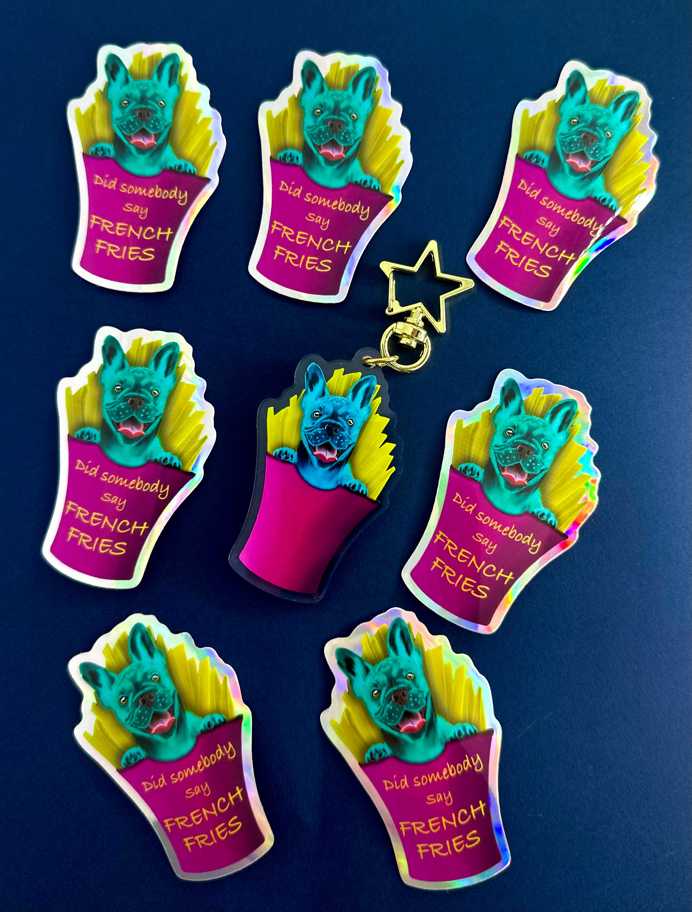 Frankie the French Bulldog in French Fries Acrylic Keychain stacked by some holographic Stickers of Frankie Blue Background