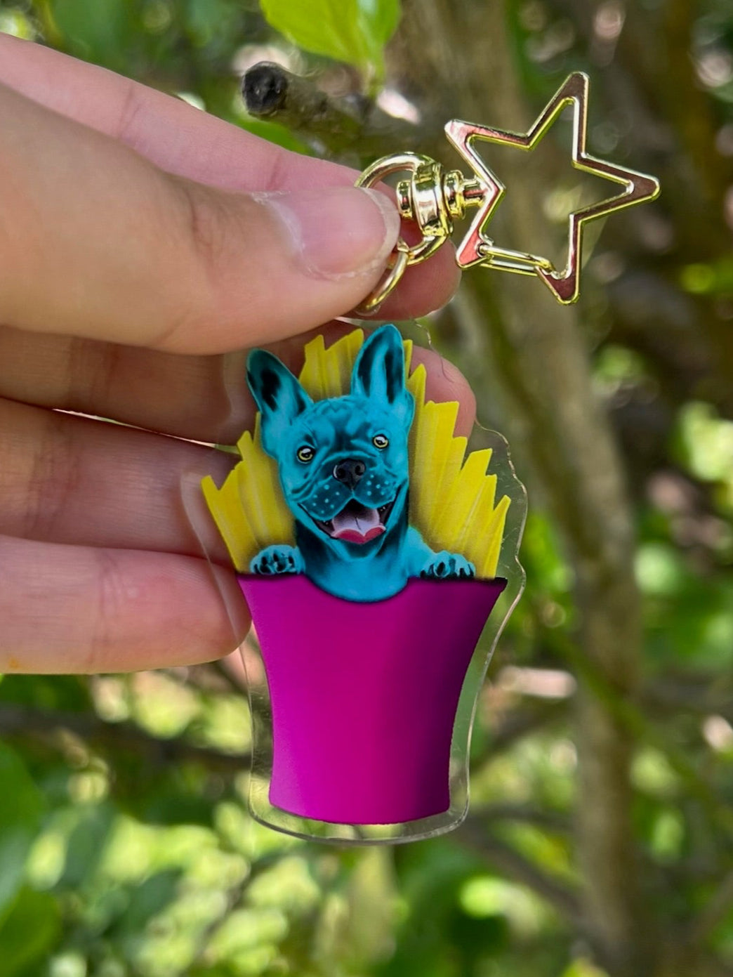 Frankie The Blue French Bulldog sitting in some French Fries Acrylic Keychain with a star clasp taken outdoors