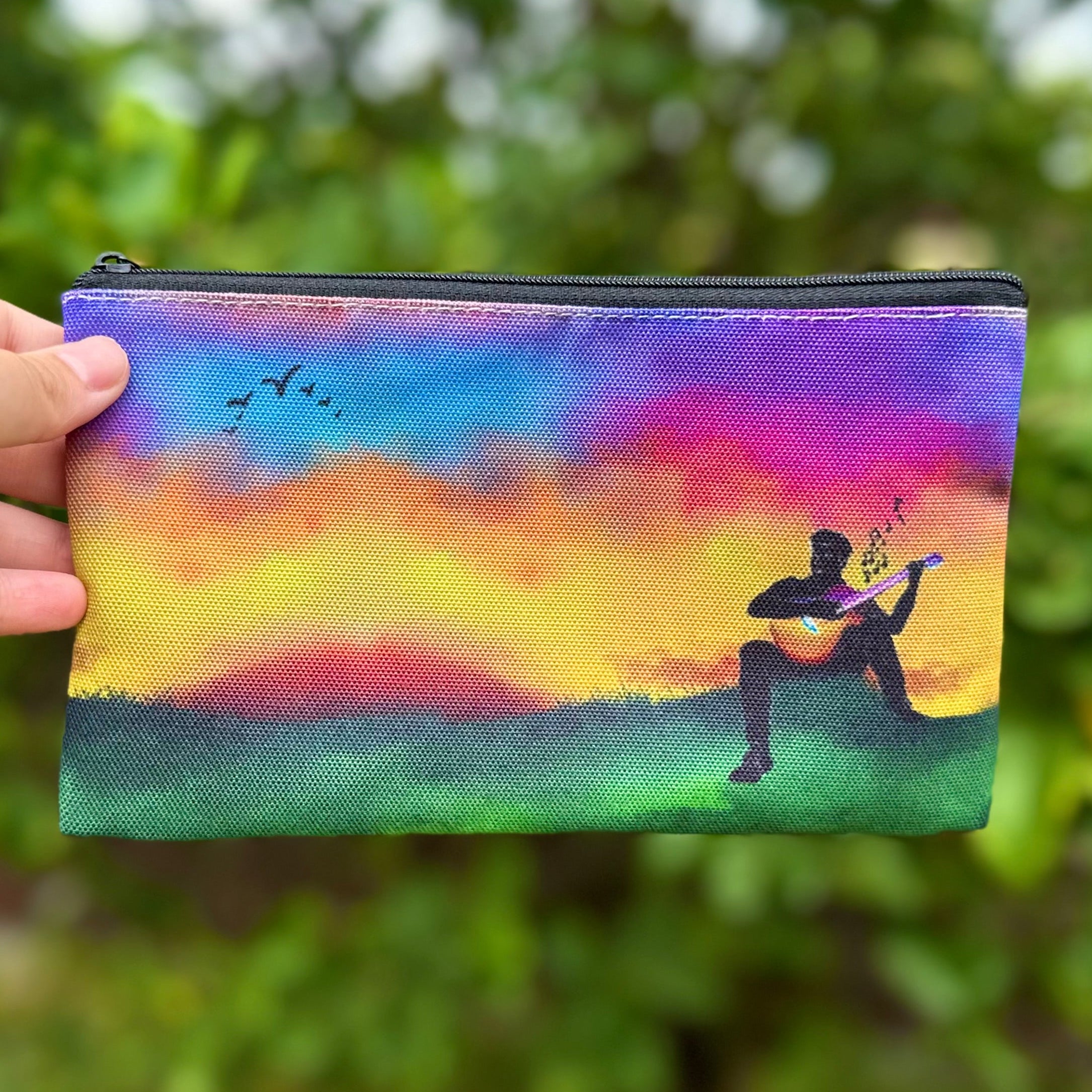 Guitartist sitting playing his rainbow guitar with a rainbow sky pouch