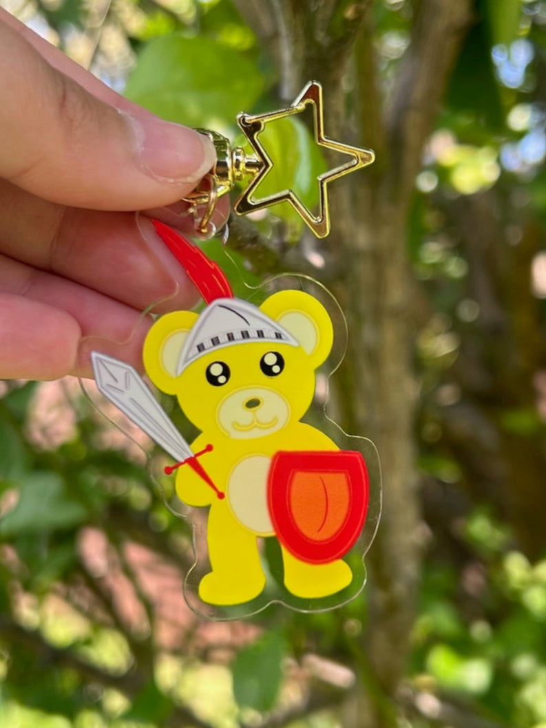 Yellow Bear Shining Knight Acrylic Keychain with a gold star clasp, kawaii artwork, taken outdoors