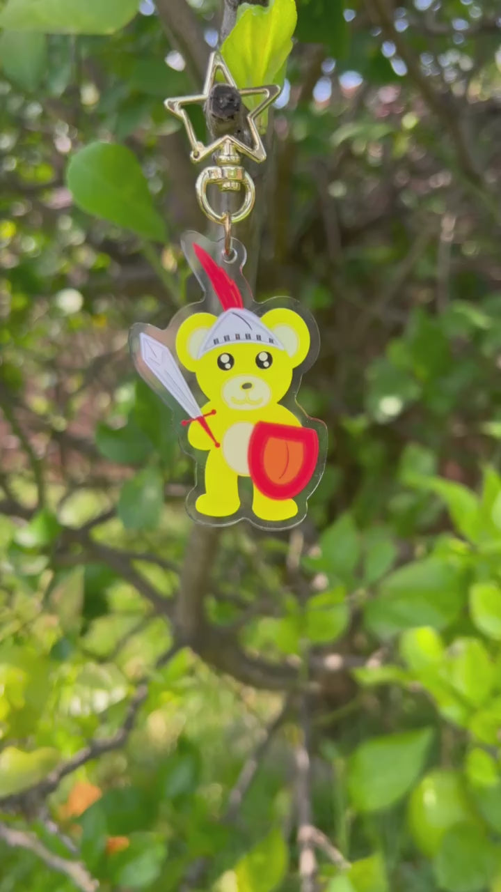 Shining Knight Yellow Bear with sword and shield acrylic keychain with a gold star clasp video taken outdoors